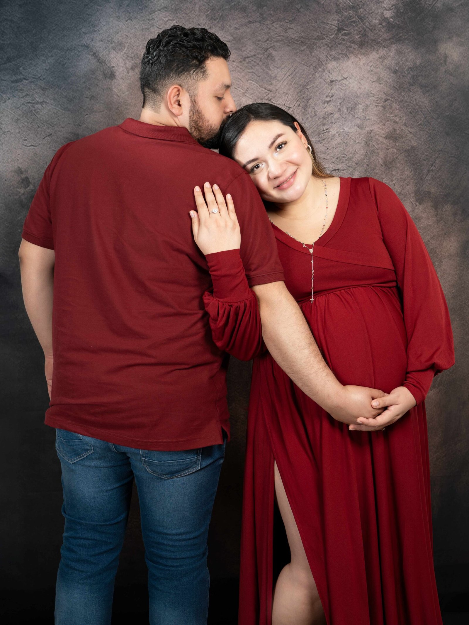 Mujer embarazada sonriendo con su esposo durante sesión de maternidad en estudio