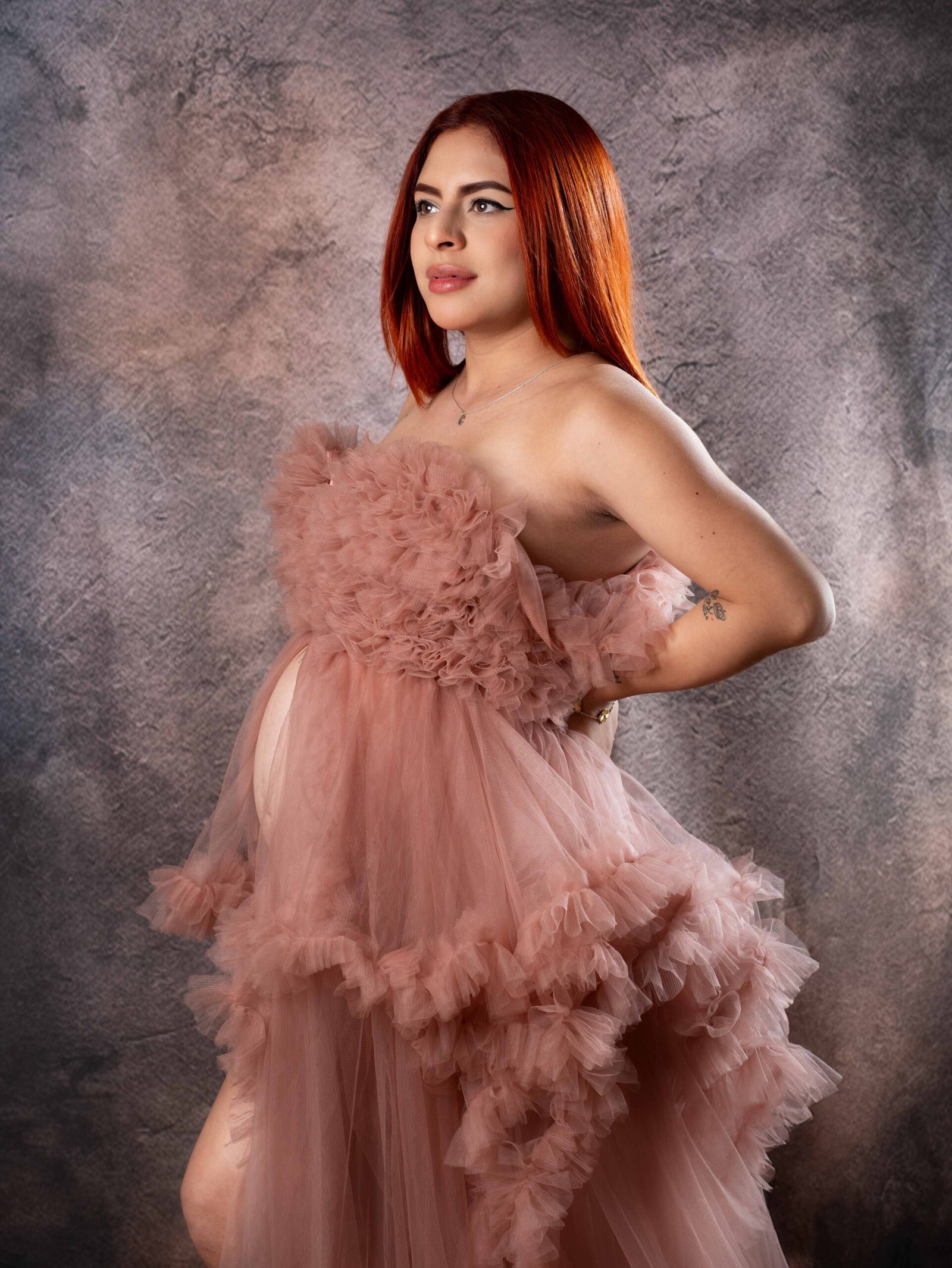 Mujer embarazada de perfil durante sesión de maternidad en estudio